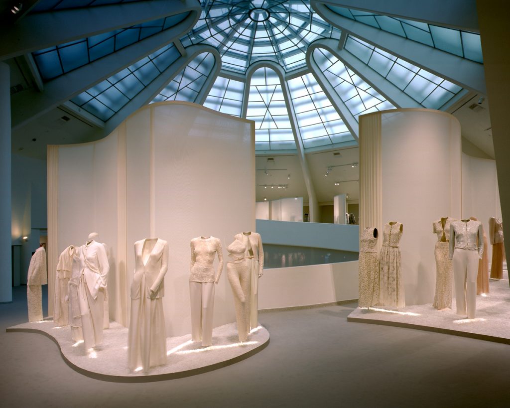 A room (high glass ceiling) featuring mannequins dressed in pale feminine garments - trouser suits, skirts, dresses