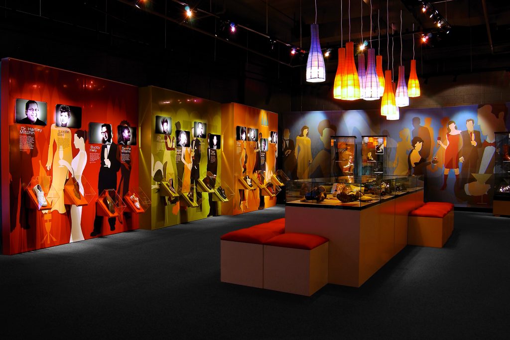 Exhibition with shoes on display against a backdrop of celebrity cutout silhouettes