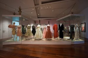 A collection of male and female evening wear garments. All in hues of red, pink, white, black and brown.