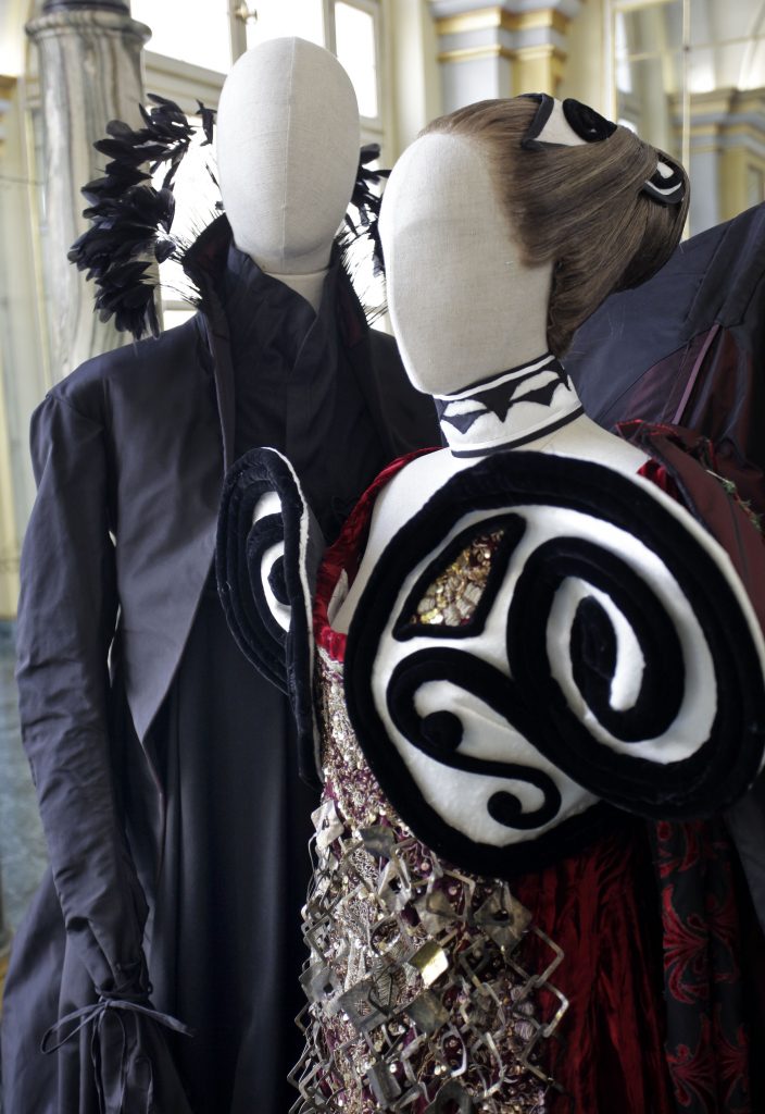 Exhibition display side view of 2 dressed mannequins in black with ornate puffed sleeves