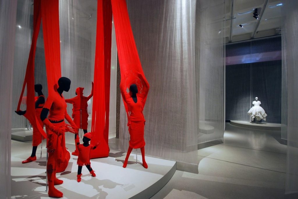 Exhibition display of mannequins dressed in red reaching up to red drapes