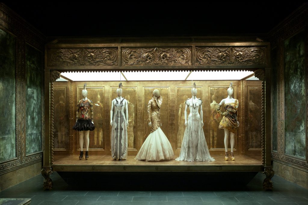 Exhibition display of five dressed mannequins within elaborate gold setting