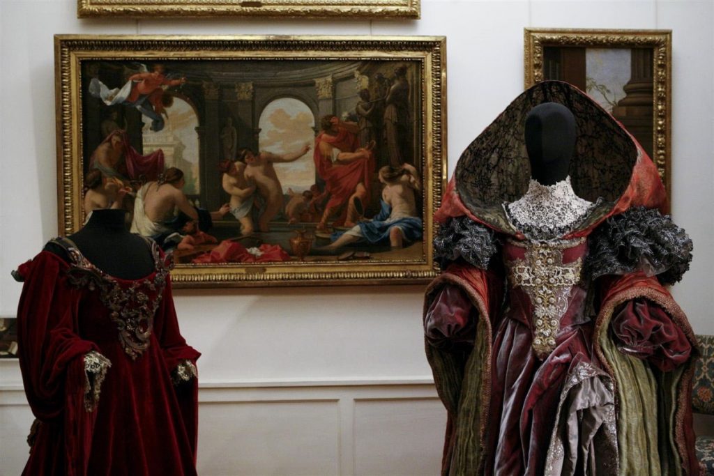 Exhibition display of dressed mannequins in 17th Century garments with hoods in front of portrait