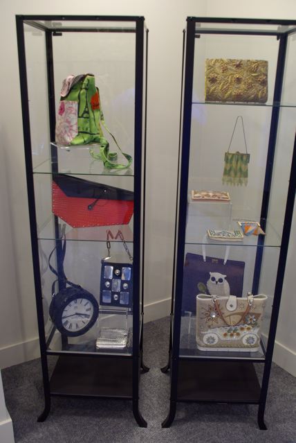 Exhibition with two glass standing cabinets displaying bags made from lucite, felt, cigarette packages, wood and glass.