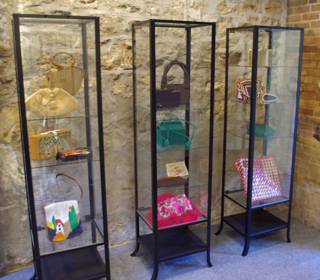 Exhibition with three glass standing cabinets displaying bags by Bags by Williwear, Marilyn Books, Paraphernalia, Enid Collins, Whiting and Davis and others.