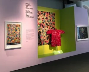 gallery view of pink t shirt with a backdrop of abstract images on the wall