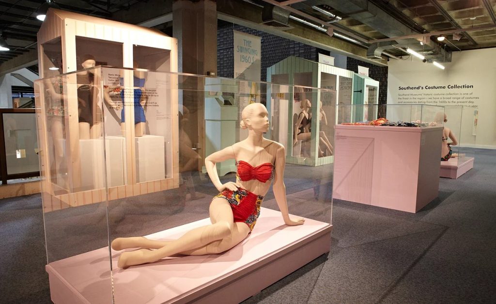Exhibition display of dressed mannequins with one sitting in foreground in swimwear