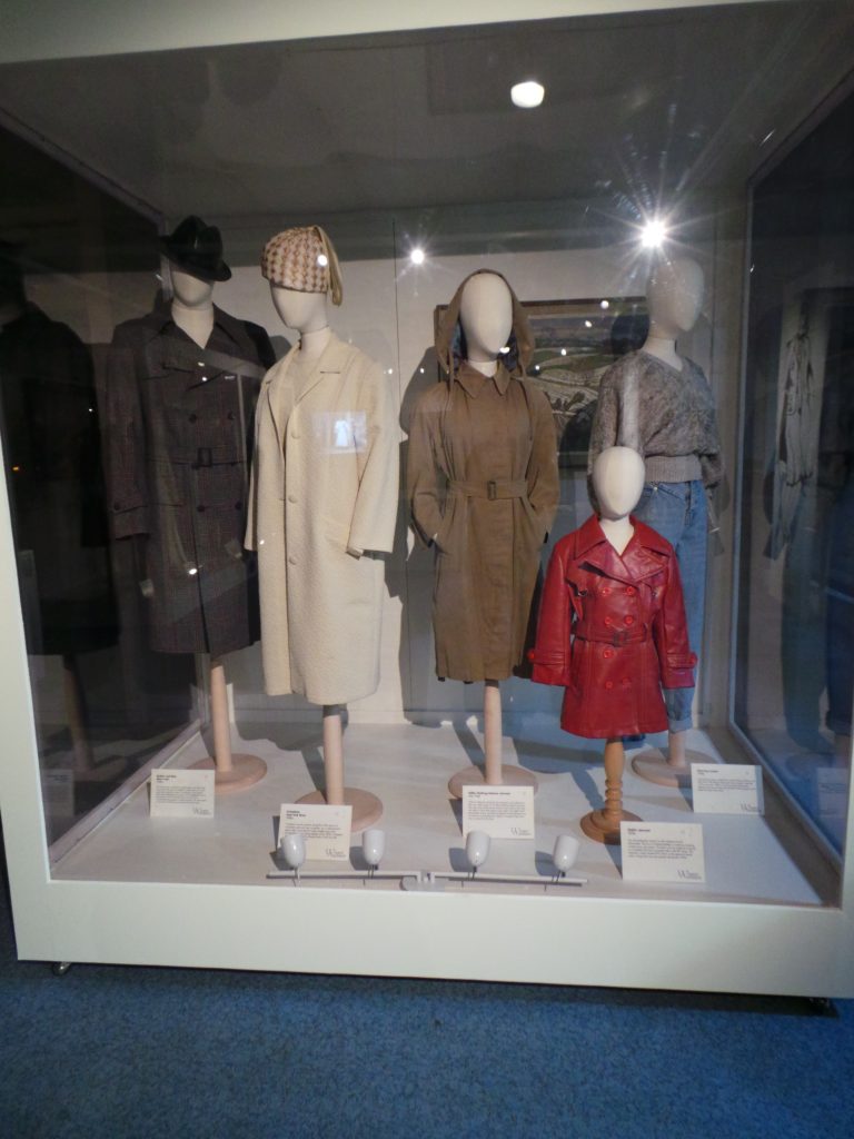 A 'family' of male and female mannequins. (Left) a full length black and brown coat, a female white coat with white hat, brown fur coat full length and (right) a child's red leather look coat.