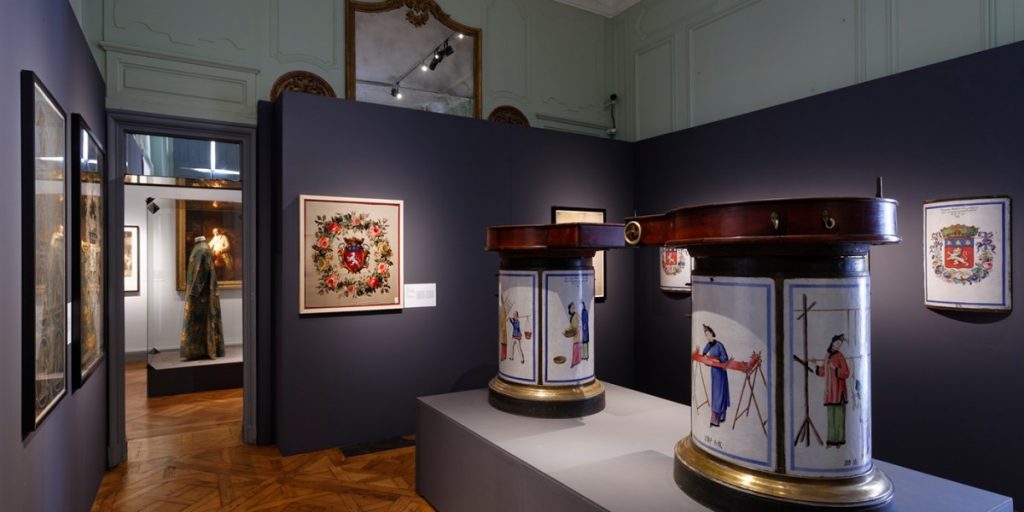 Exhibition display of decorated plinths with dressed mannequin in historic garments in background