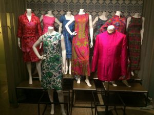 A group of eight dresses displayed on mannequins and one coat on a tailor's dummy, all in contrasting Liberty prints