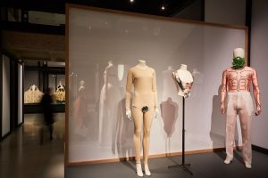 A display of two female and one male mannequins, dressed in pale garments emphasising the attributes of the physical body