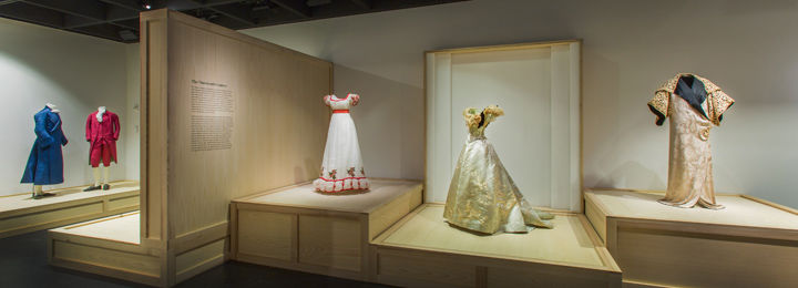 Women's and men's dress are displayed on wooden plinths resembling crates or large-scale packing boxes