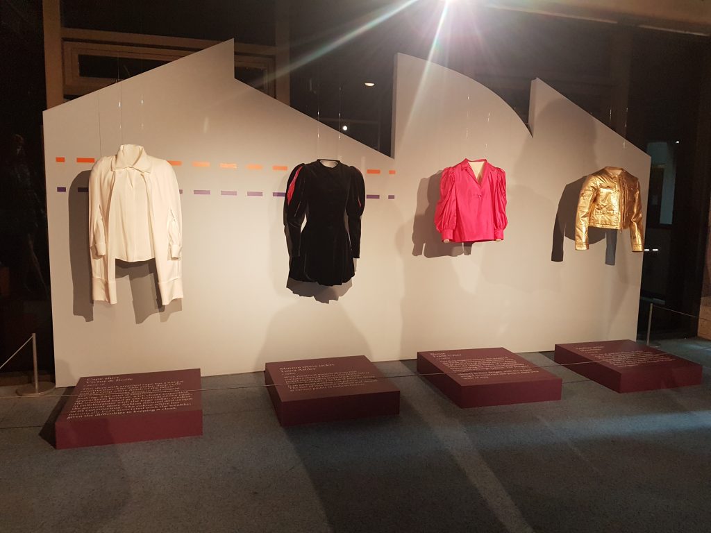 four garments displayed on a wall in hues of white, black, pink and yellow.