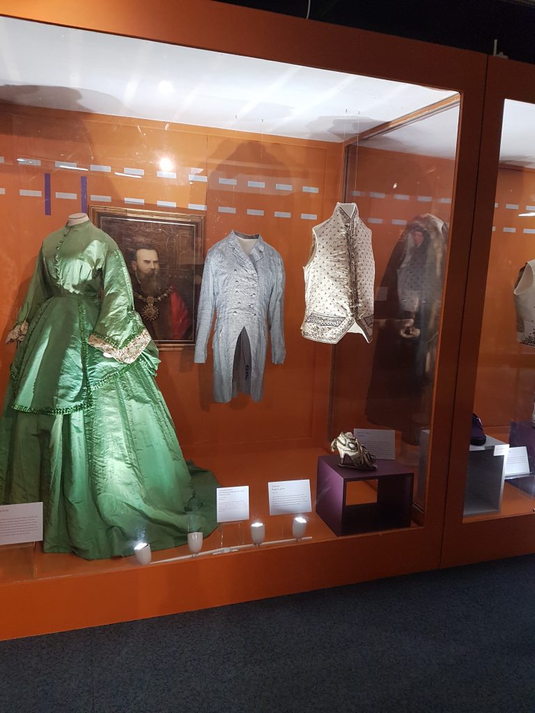 A green ballgown displayed alongside, grey, blue and white menswear.