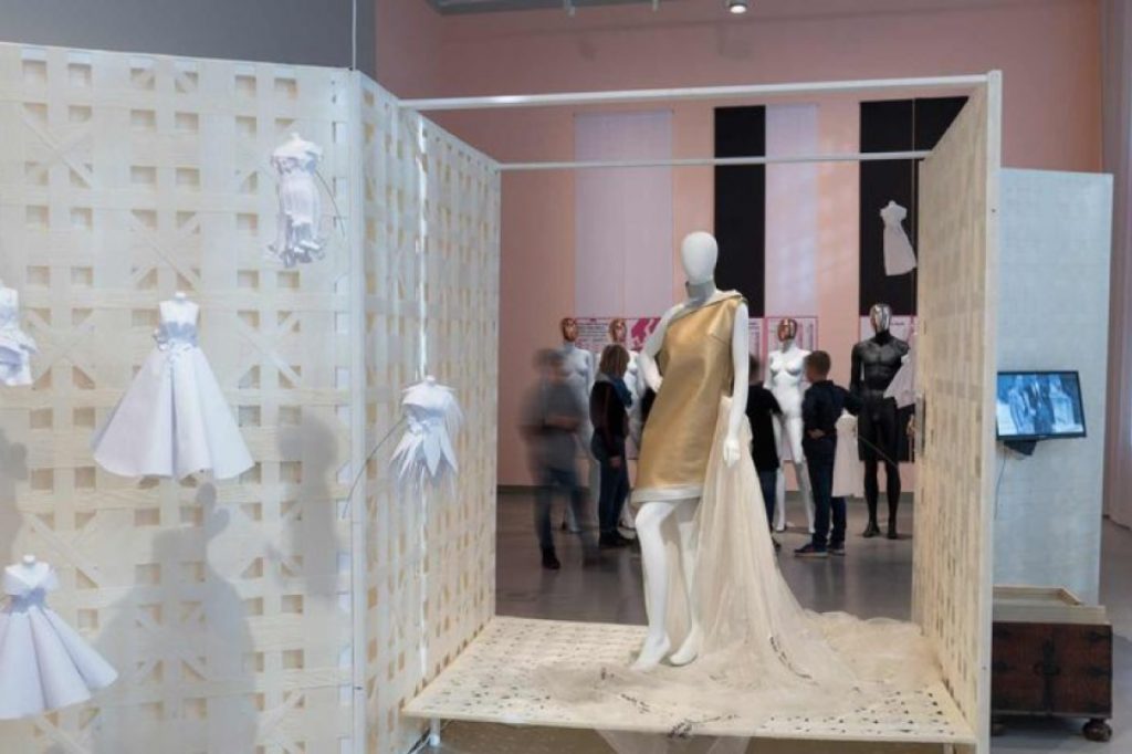 Exhibition display of dressed mannequins with small wedding dresses suspended to the side