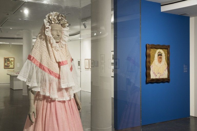 Female mannequin wearing a white lace shall featuring a pink ribbon. The mannequin is also wearing silver beaded flowers on top of it's head and a light pink long skirt.