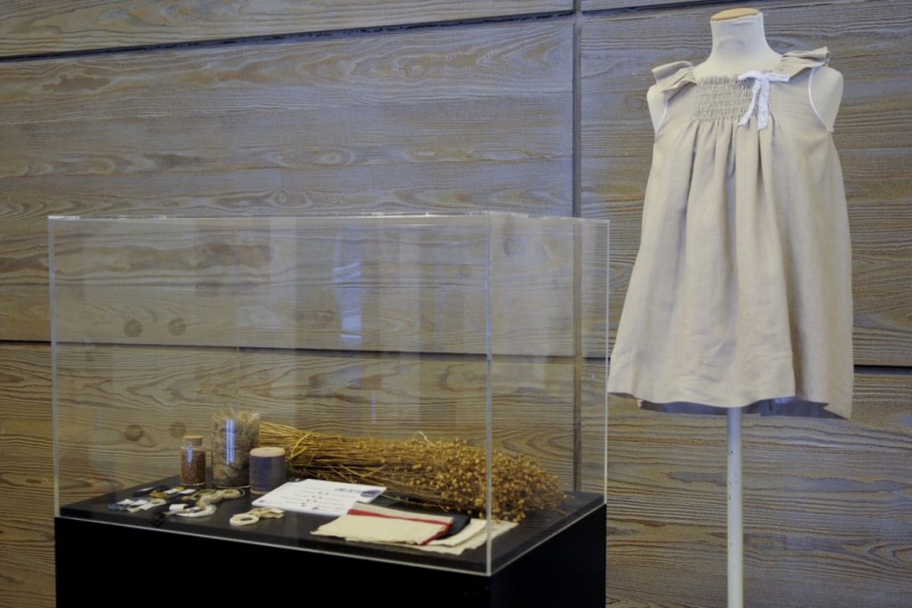 Exhibition display of dressed mannequin torso in smock beside a glass case of objects