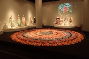 Exhibition display of dressed mannequins around a circular floor display of flowers