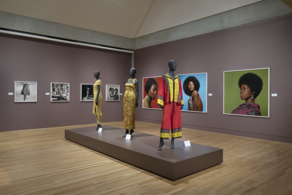 Exhibition display of dressed mannequins with portraits in background