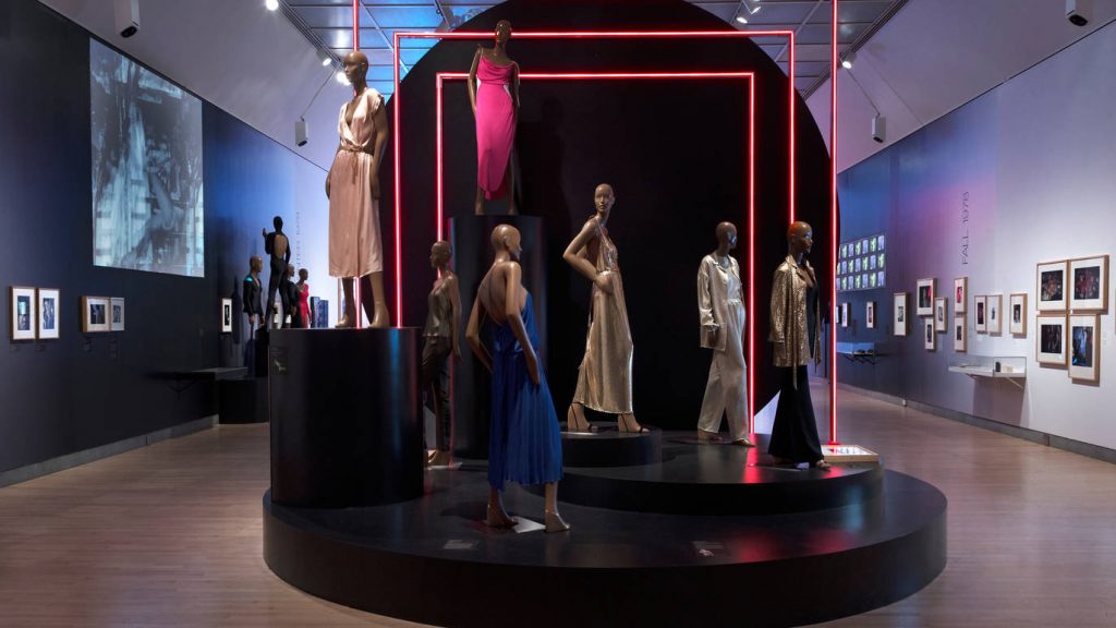 Exhibition display of dressed mannequins on a raised plinth with neon lighting