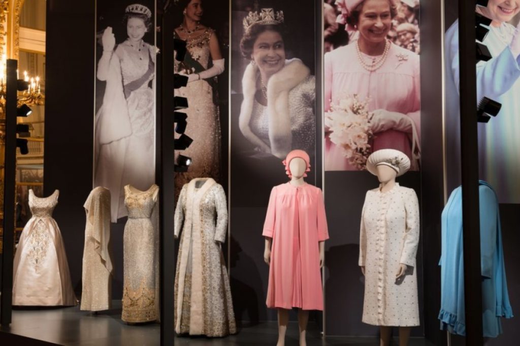 Exhibition display of dressed mannequins with Queen Elizabeth II garments against a backdrop