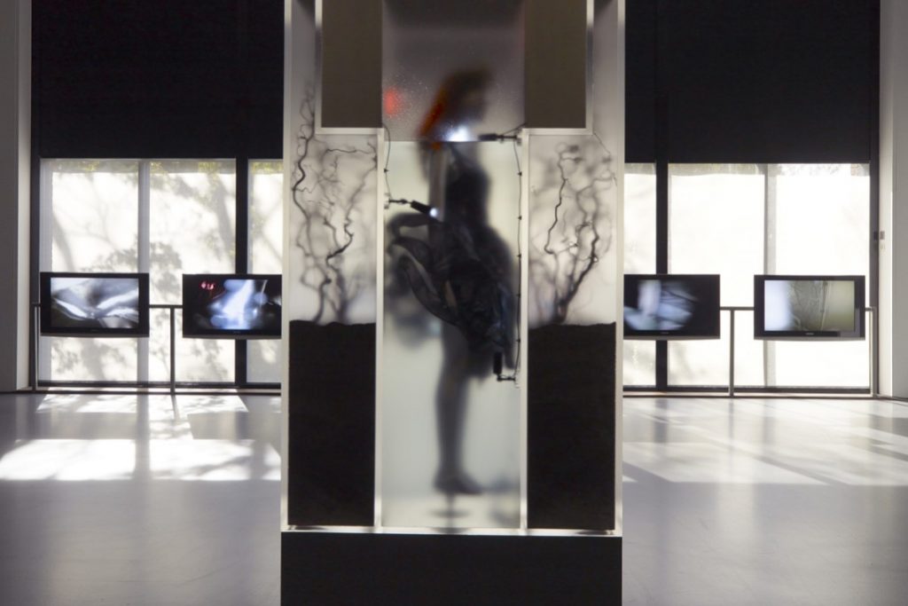Exhibition display of silhoutted dressed mannequin and multiple tv screens