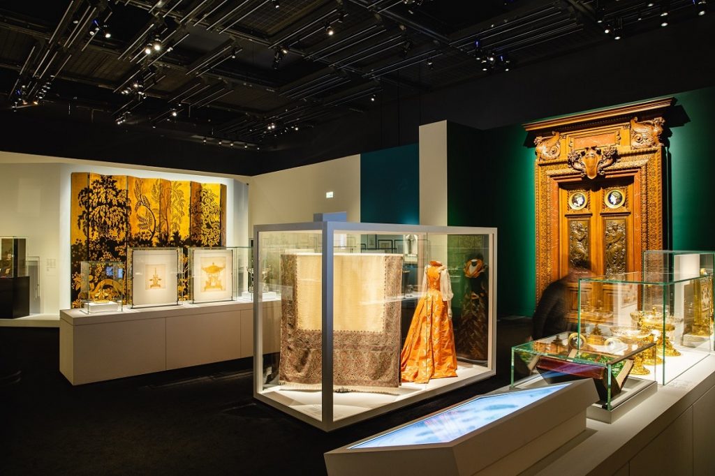 Exhibition display of textiles, ornate objects and dressed mannequins in cases