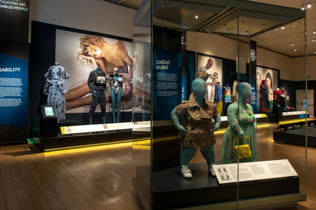 Exhibition display of dressed mannequins with large artwork in background