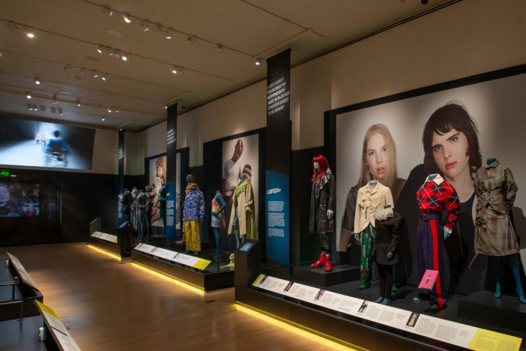 Exhibition display of dressed mannequins with large artwork in background
