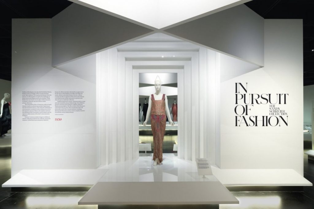 Exhibition display of dressed mannequin in a doorway setting with exhibition name and captions on wall