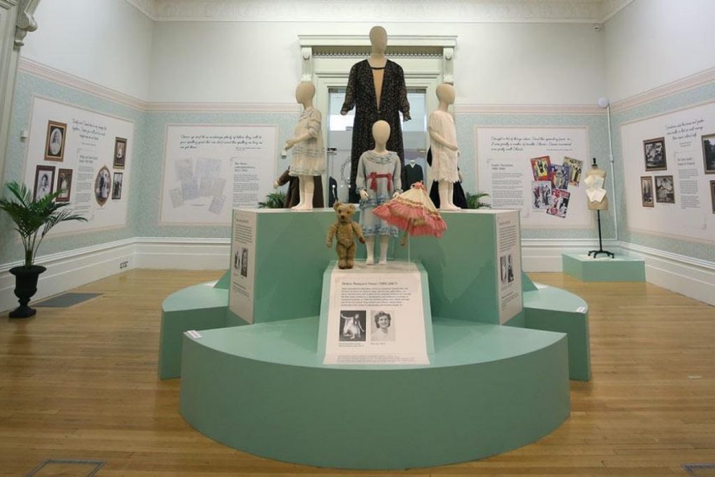 Exhibition display of dressed mannequins, some of children on green plinth