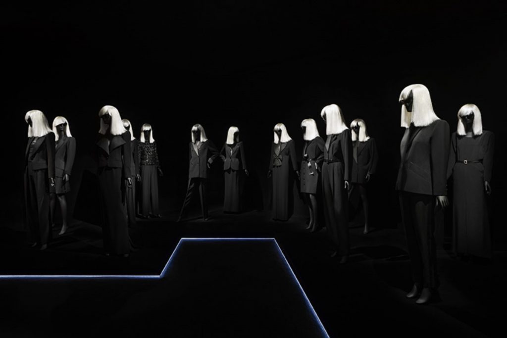 Exhibition display of dressed mannequins with white wigs in dark background