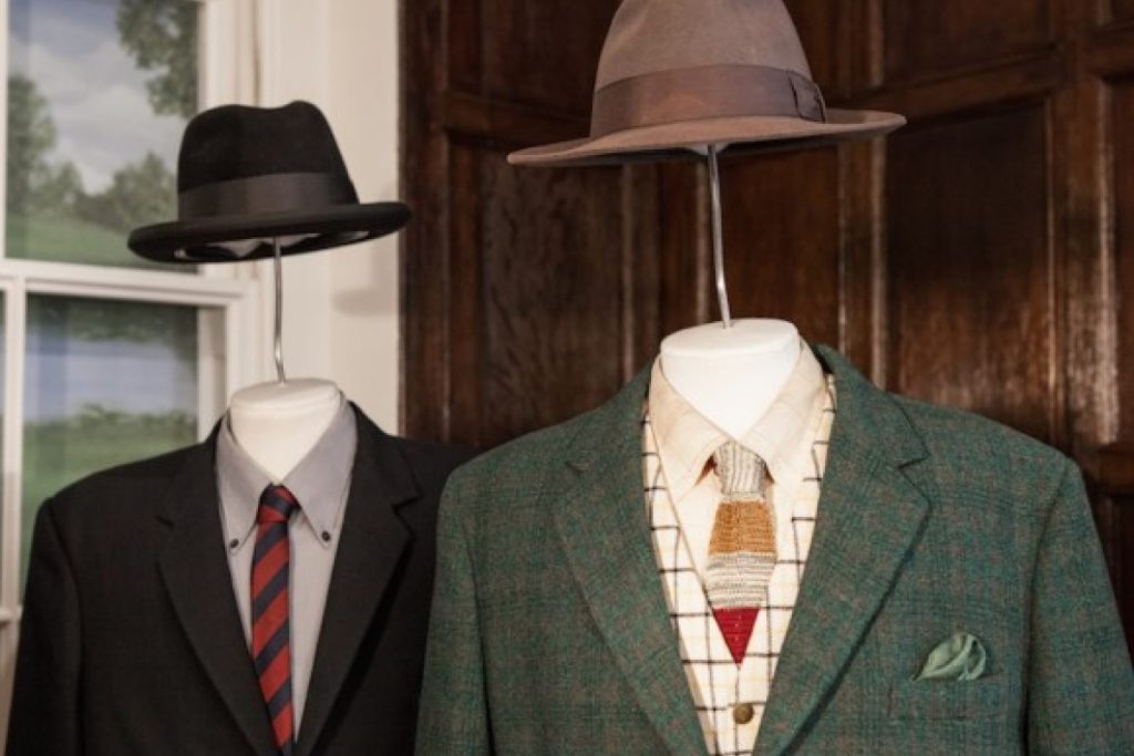 Exhibition display of men's suit and tie attire with trilby hats suspended on wire above