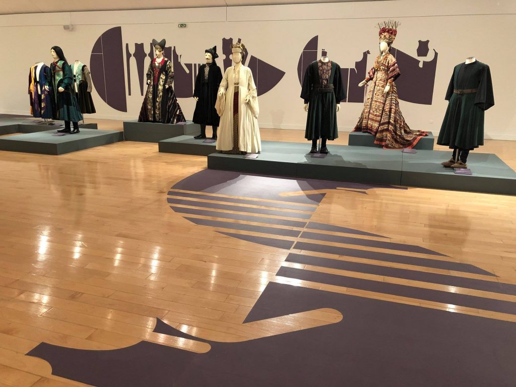 Exhibition display of dressed mannequins with wooden patterned floor in foreground