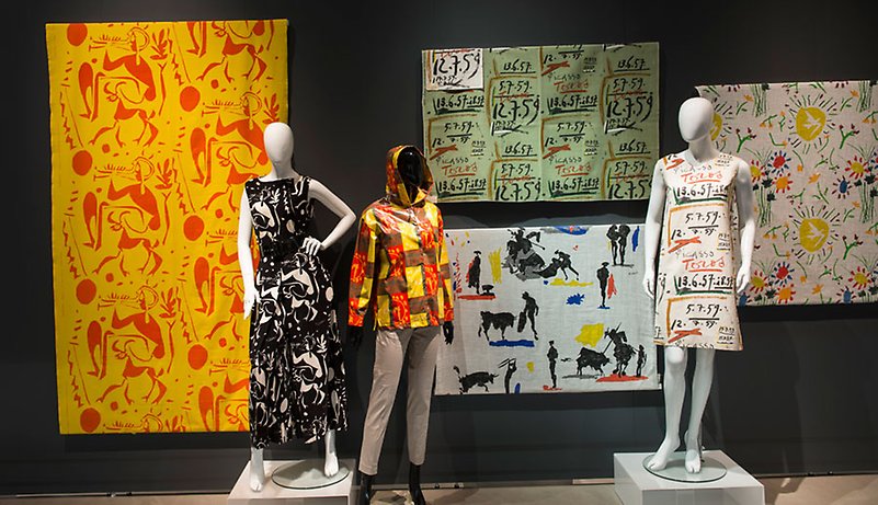 Exhibition display of dressed mannequins with backdrop of printed textiles