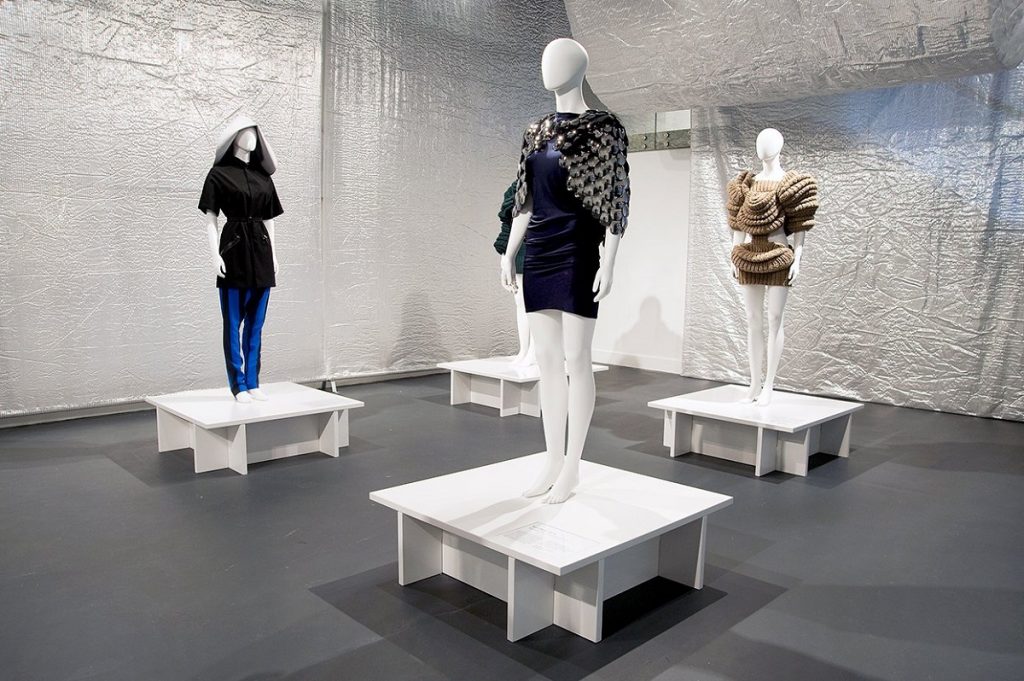 Exhibition display of dressed mannequins on white pedestals