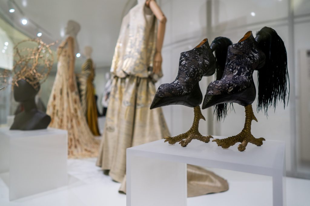 Exhibition display of dressed mannequins with black bird style shoes, feather-adorned and with birds' feet as heels in foreground