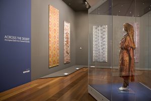 Exhibition display of textiles on wall and dress inside glass vitrine