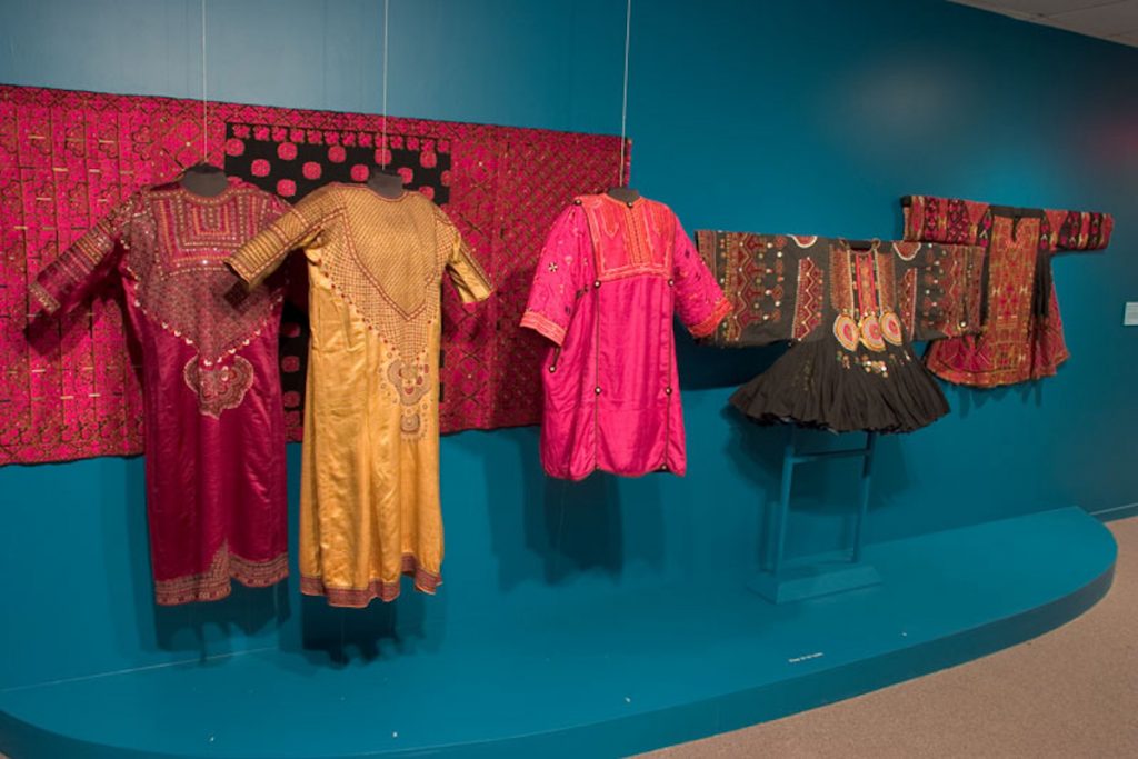 Exhibition display of dress hung in front of textile panel against blue wall