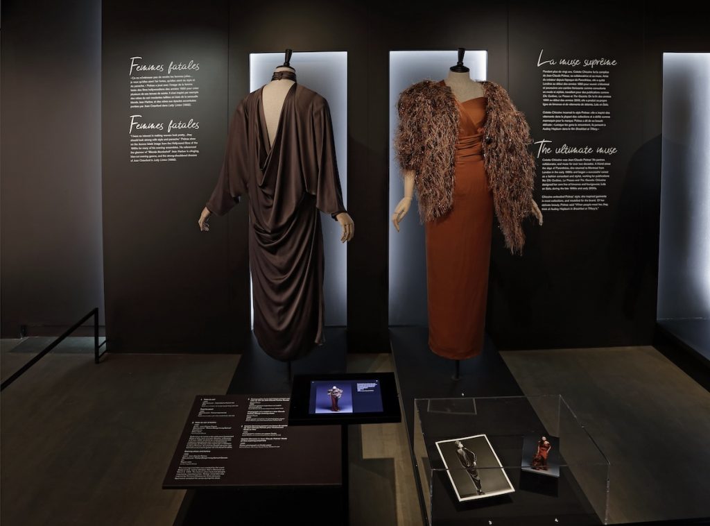 Exhibition display of dress of two drsses on headless mannequins. Text panels displayed behind the dresses