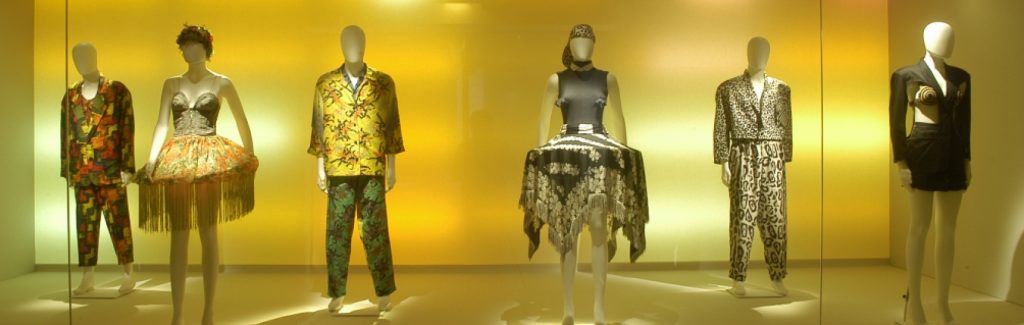 Exhibition display of dressed mannequins with gold backdrop