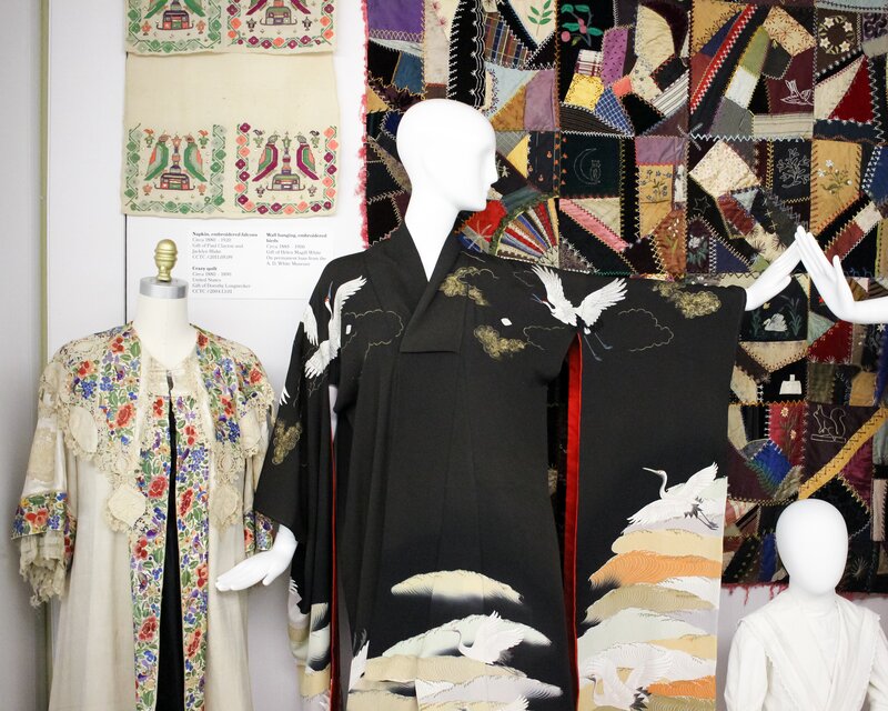 Exhibition display of dressed mannequins with patchwork fabric hanging behind