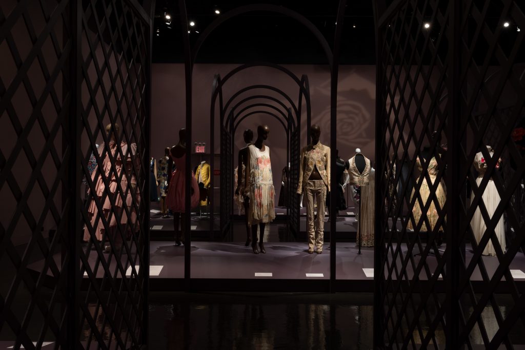 Exhibition display of dressed mannequins behind a trellis