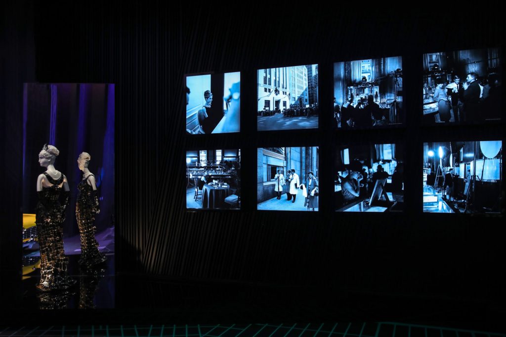 Exhibition display of dressed mannequin in front of a series of screens showing film 'Breakfast at Tiffany's'