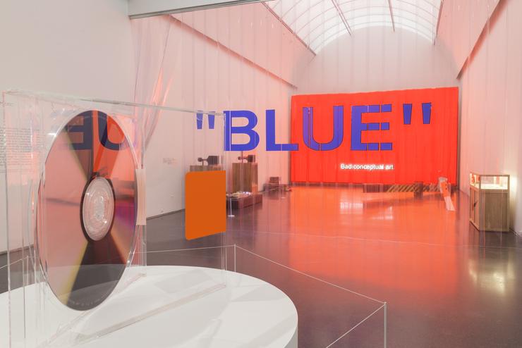 Exhibition display of dressed mannequins with red wall and the text 'blue' in blue writing