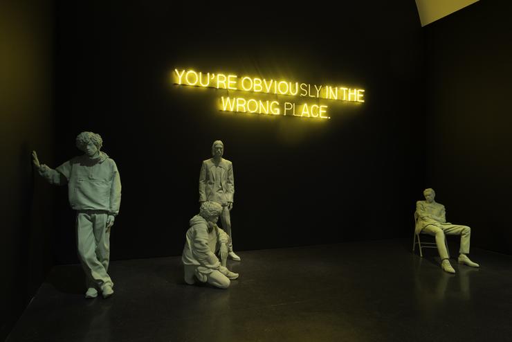 Exhibition display of dressed mannequins with illuminated writing 'you're obviously in the wrong place'