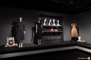 Three mannequins displaying two dresses and a skirt and jacket stand alongside three shelves of hats, bags and shoes
