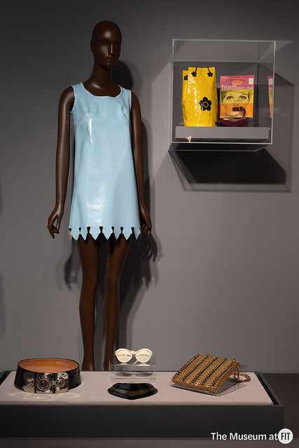 A mannequin wearing a pale blue mini dress, alongside accessories including a belt, glasses and bags