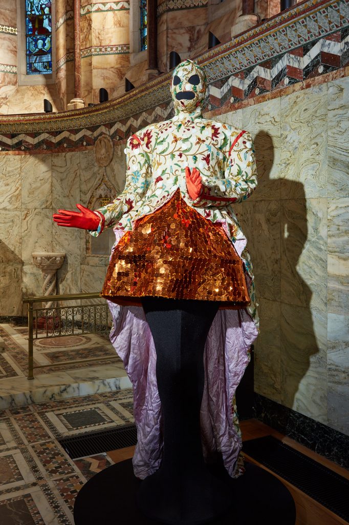 Exhibition display in church of dressed mannequin of Leigh Bowery with arms raised