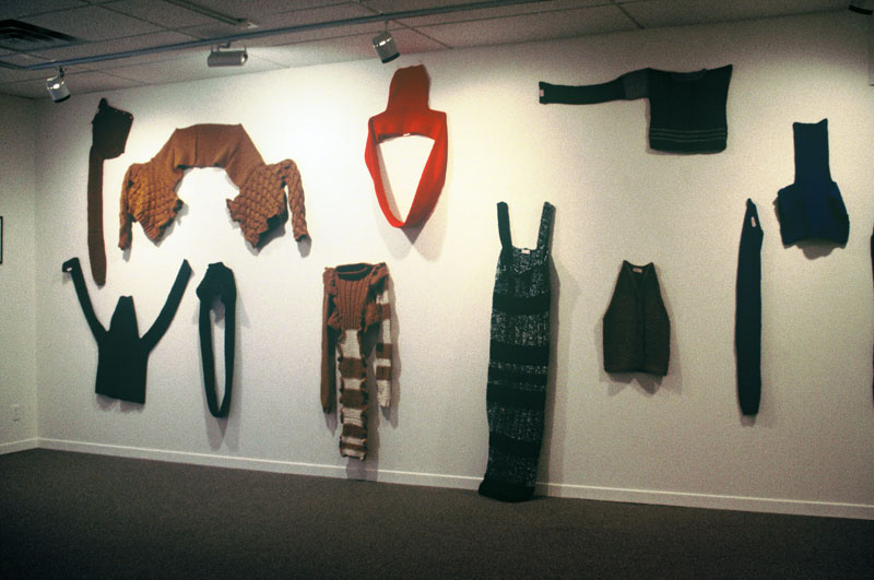 Exhibition with knitwear garments hanging on the wall.